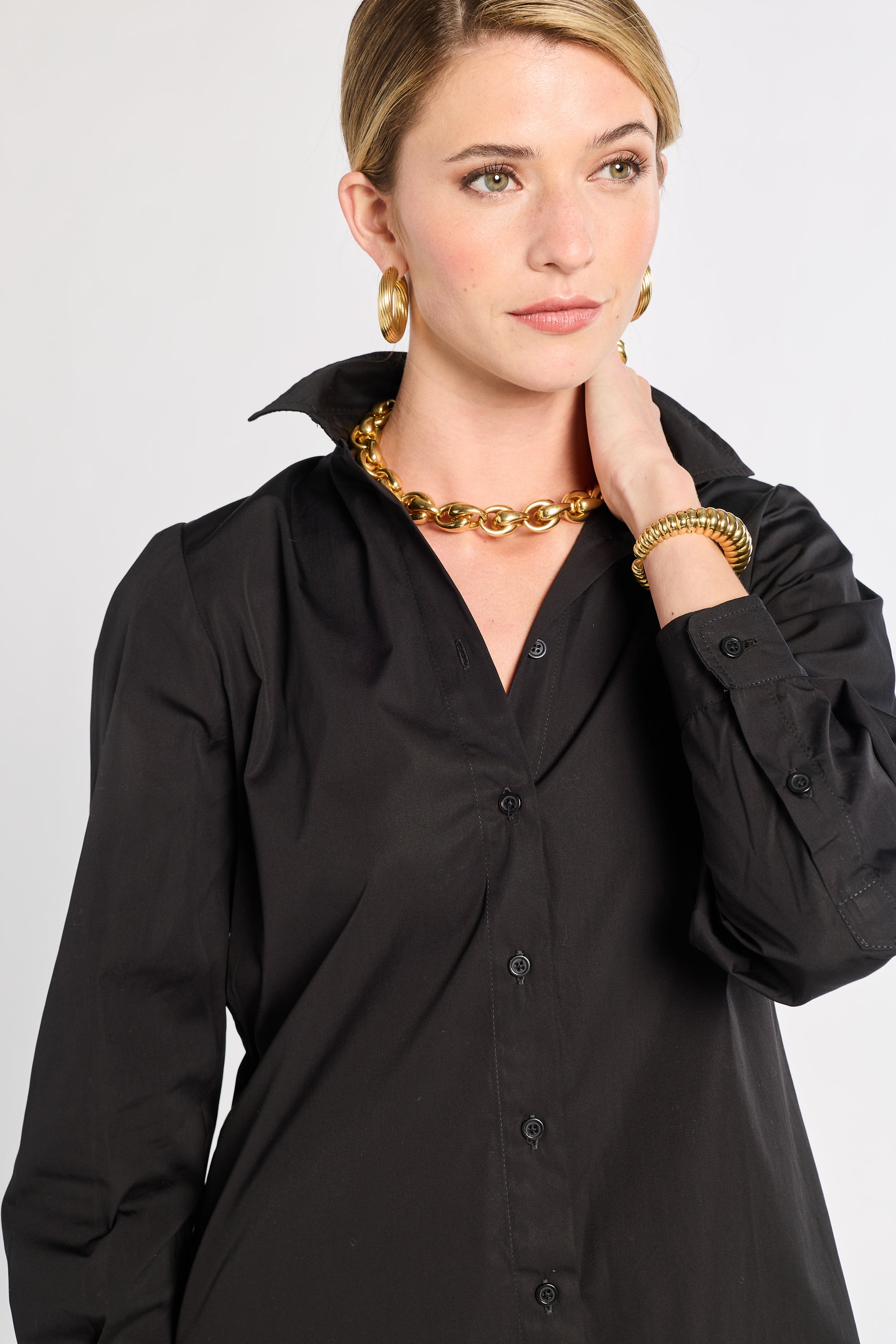 Woman wearing a black shirt with a gold necklace and bracelet on a white background