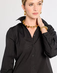 Woman wearing a black shirt with a gold necklace and bracelet on a white background