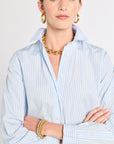 Woman wearing a light blue striped shirt with gold jewelry against a white background