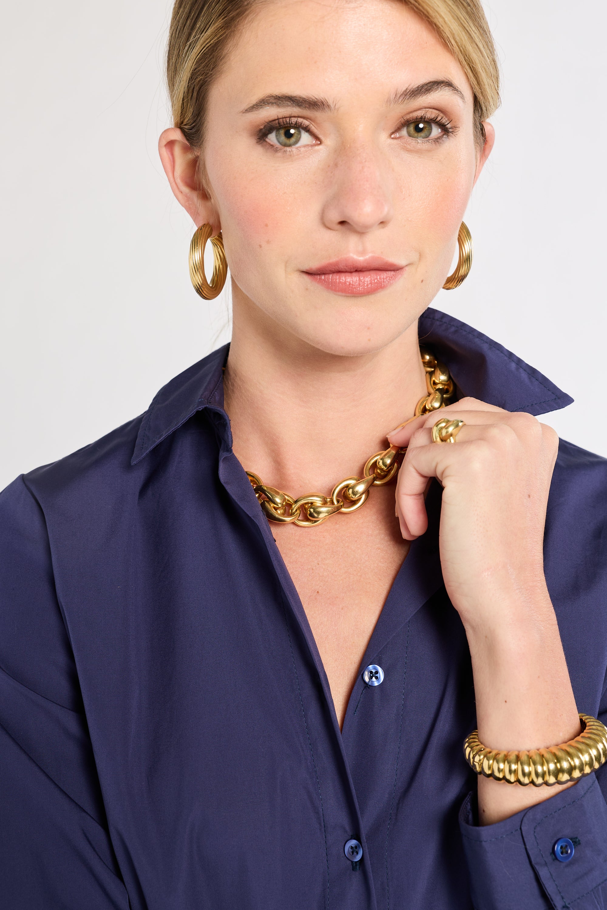 Woman wearing gold jewelry including a necklace, hoop earrings, and bracelet against a white background