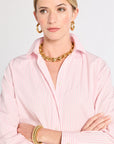 Woman wearing a pink shirt with gold jewelry on a light gray background