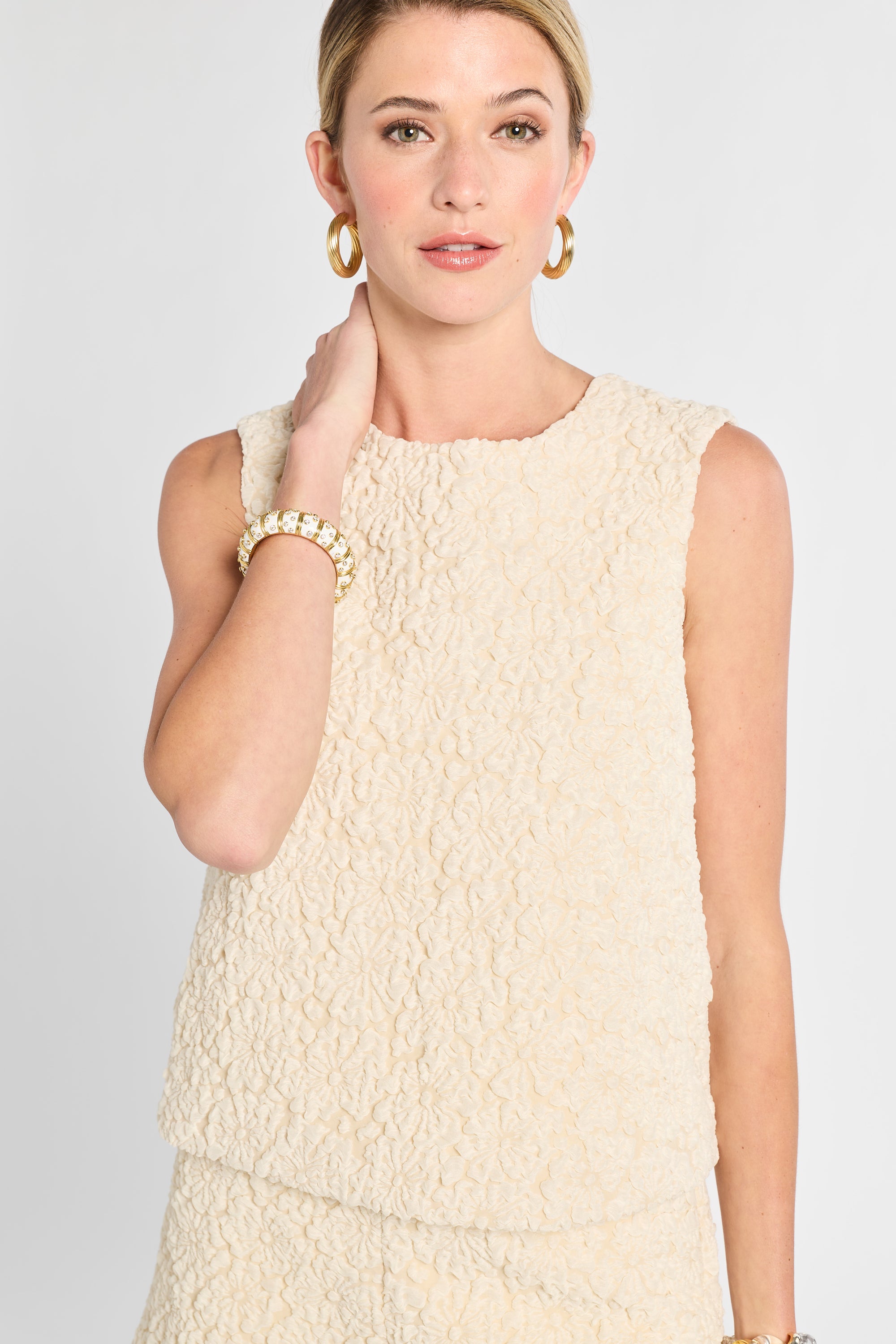 Woman wearing a textured beige sleeveless top against a plain background