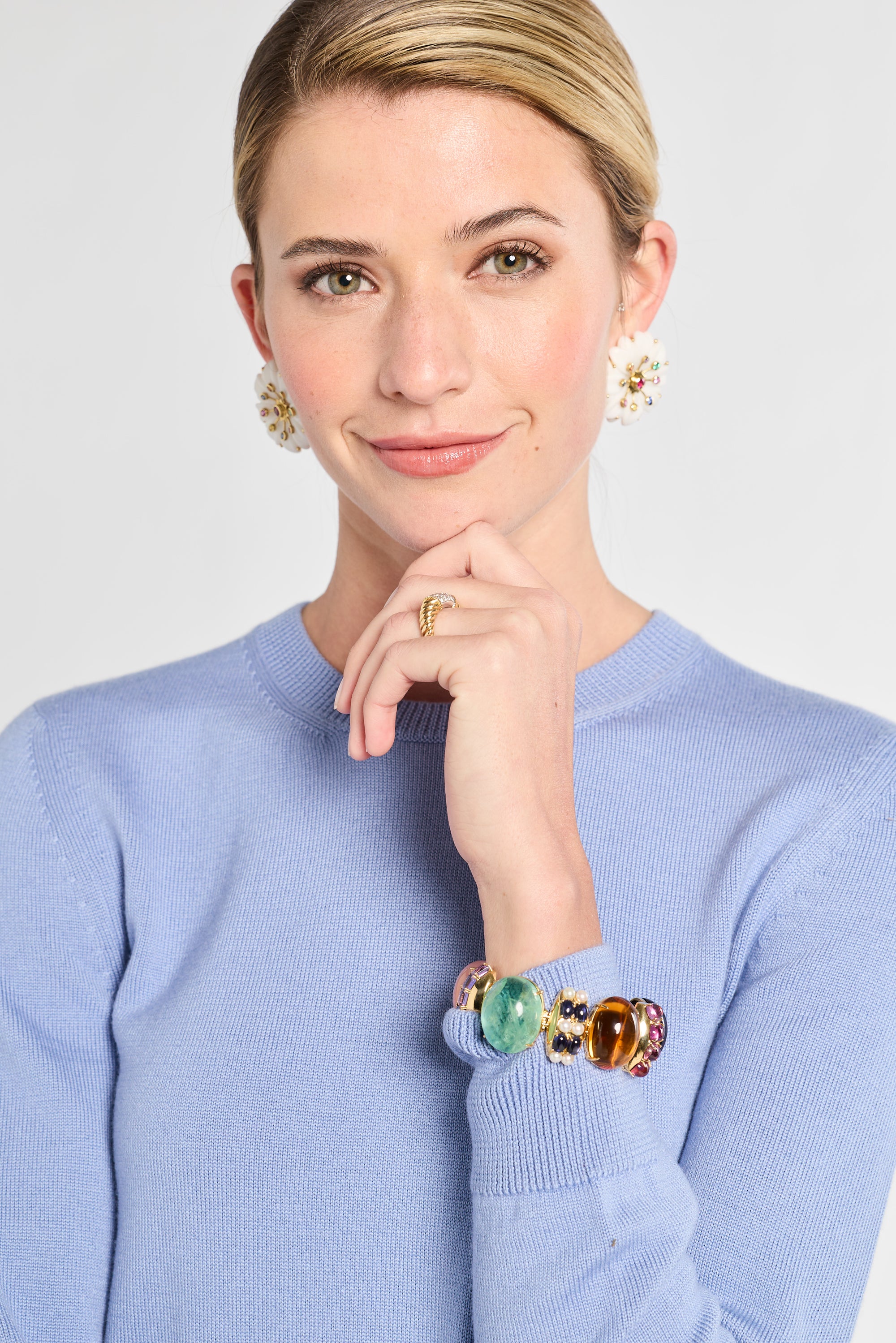 Woman wearing a blue sweater with a colorful bracelet on her wrist, against a plain background.