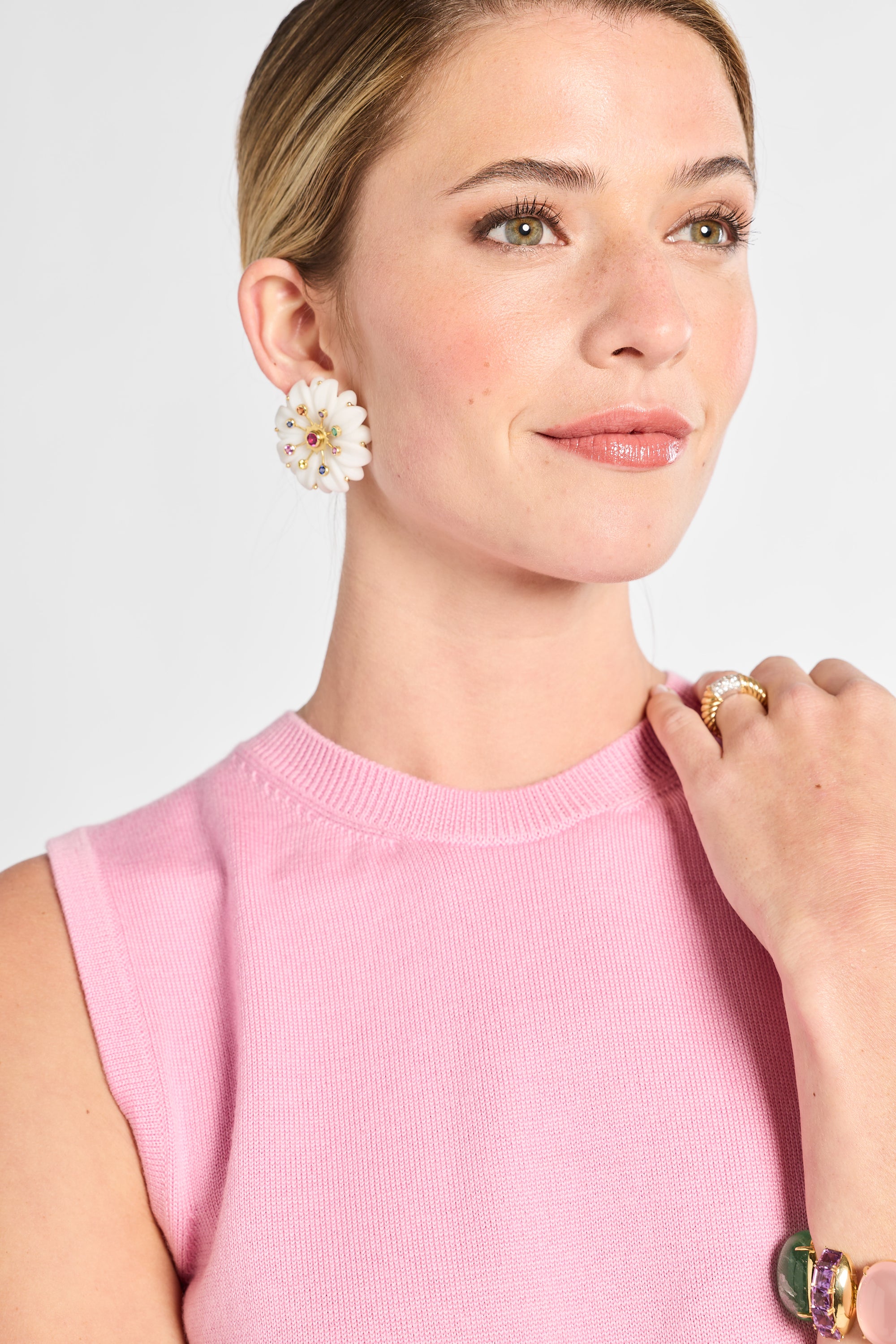 Woman wearing a pink sleeveless top with floral earrings and a ring on a light gray background