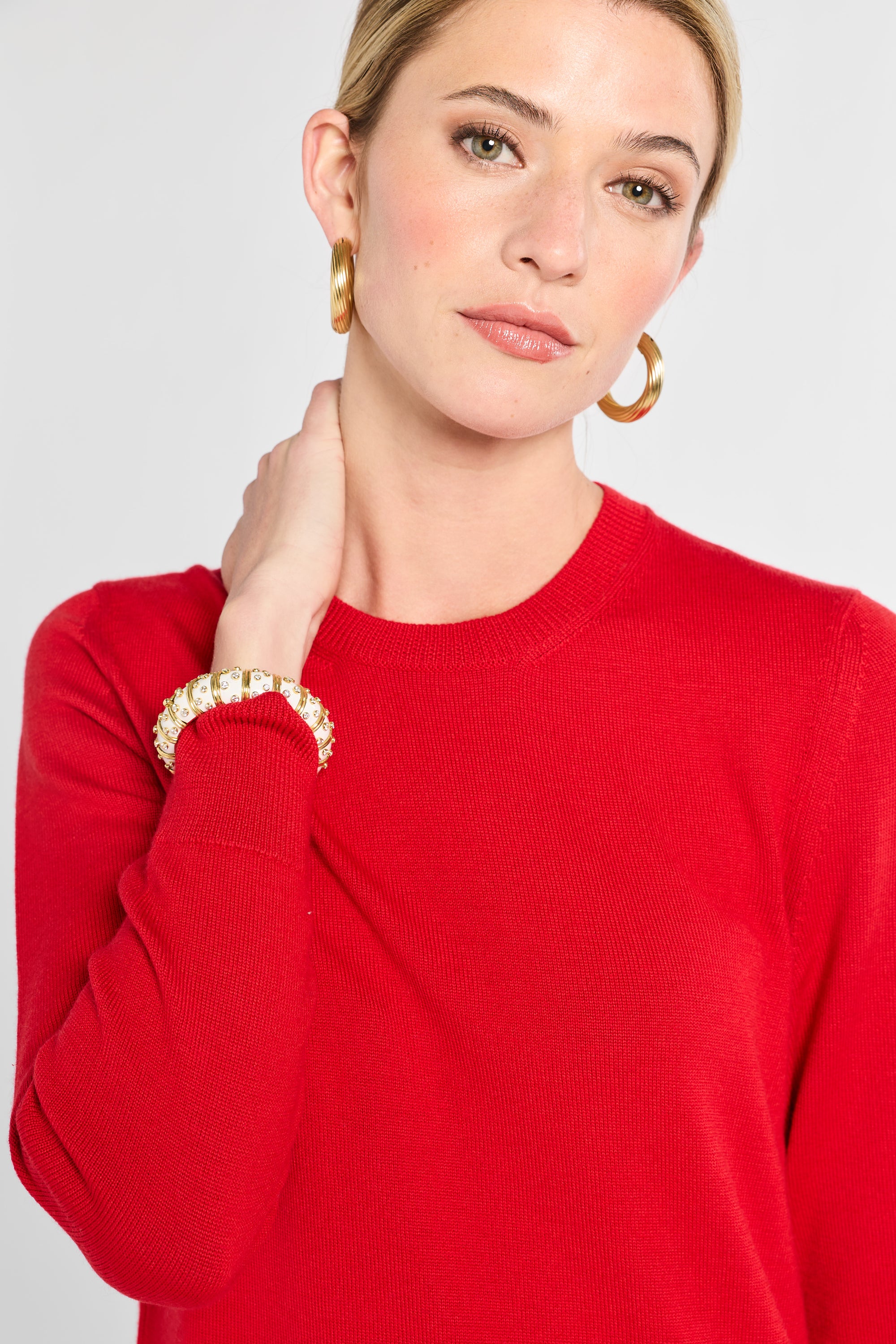 Woman wearing a red sweater with gold jewelry on a plain background