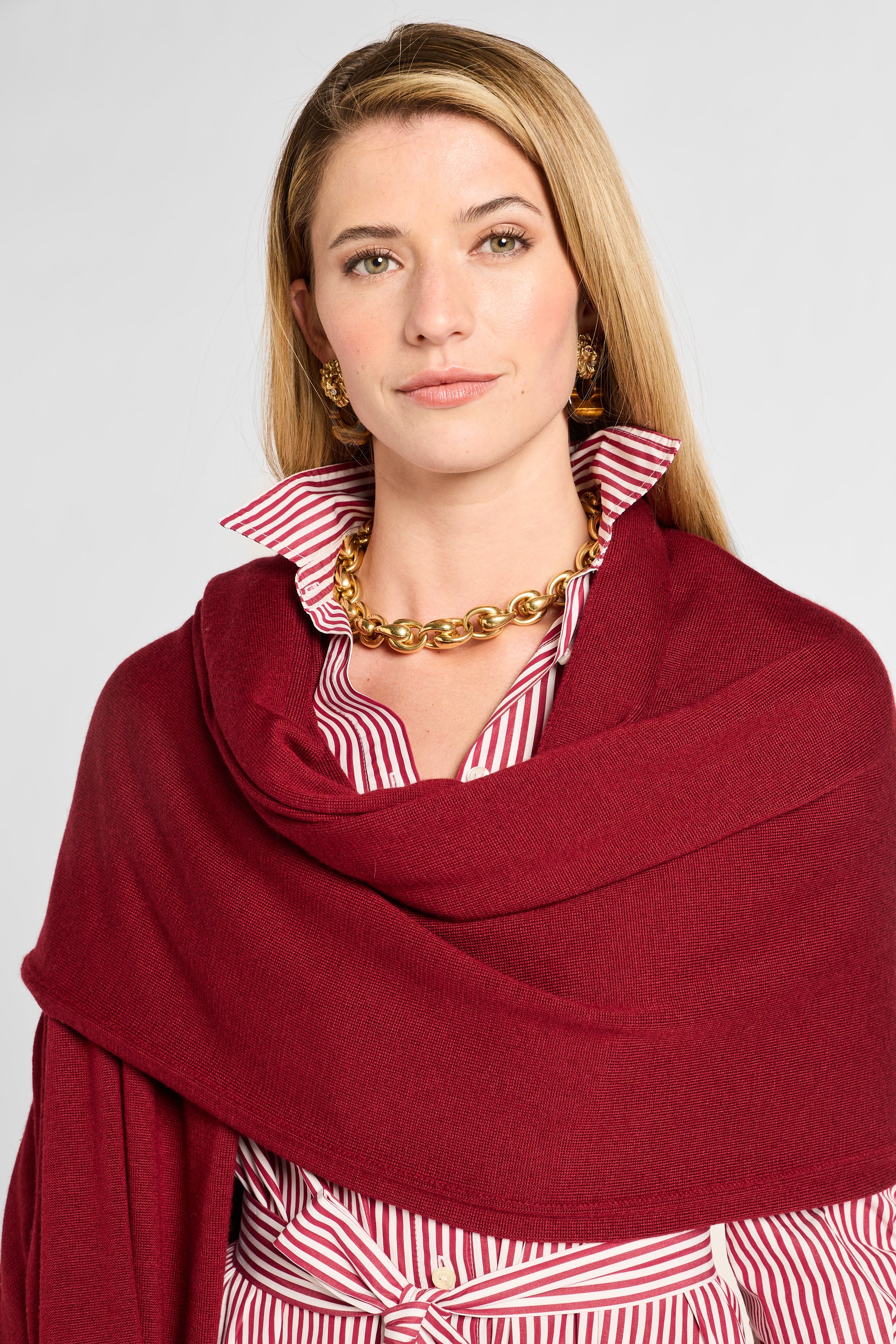 Woman wearing a red scarf over a striped shirt with a plain background