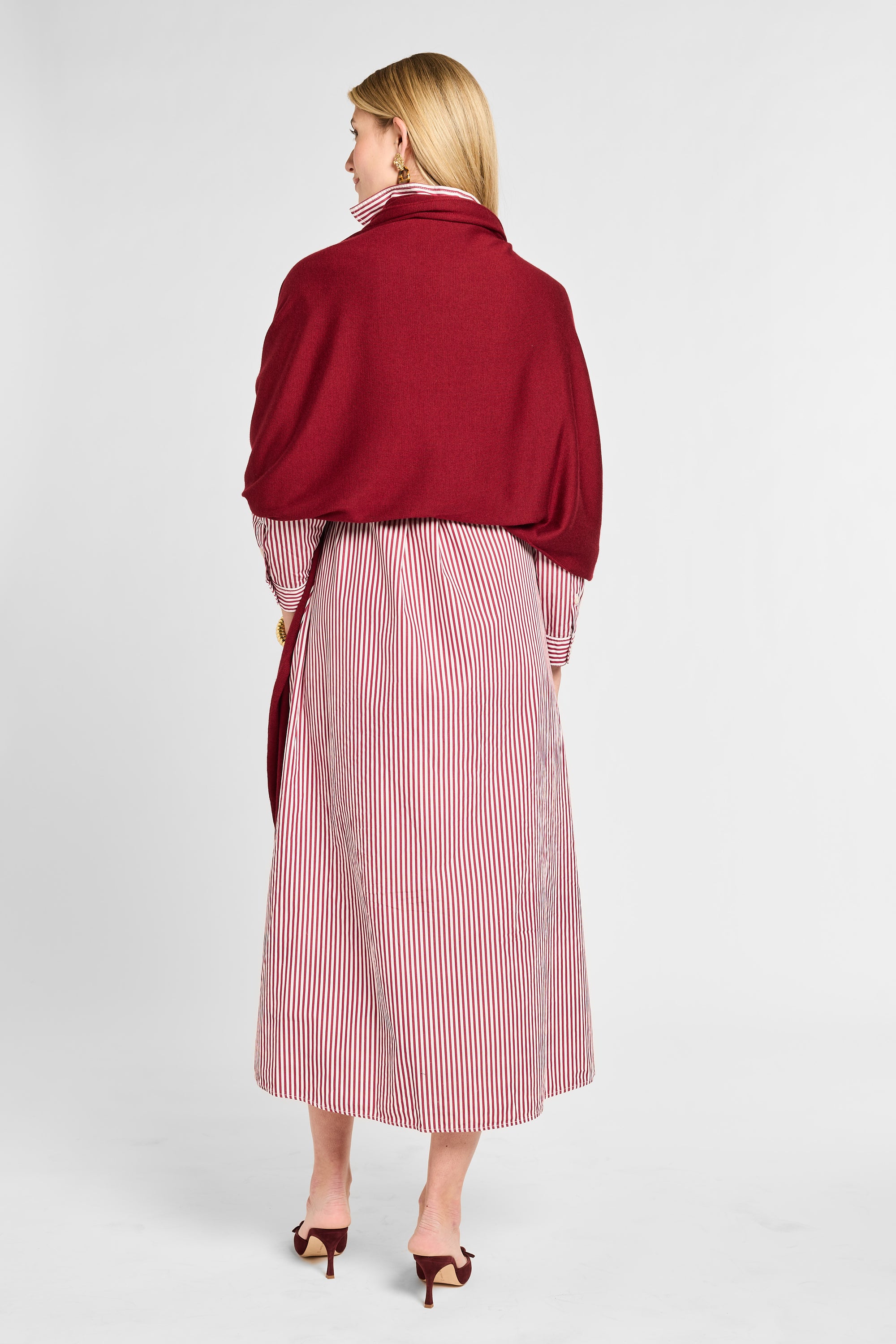 Woman wearing a red coat over a pink and white striped dress on a white background