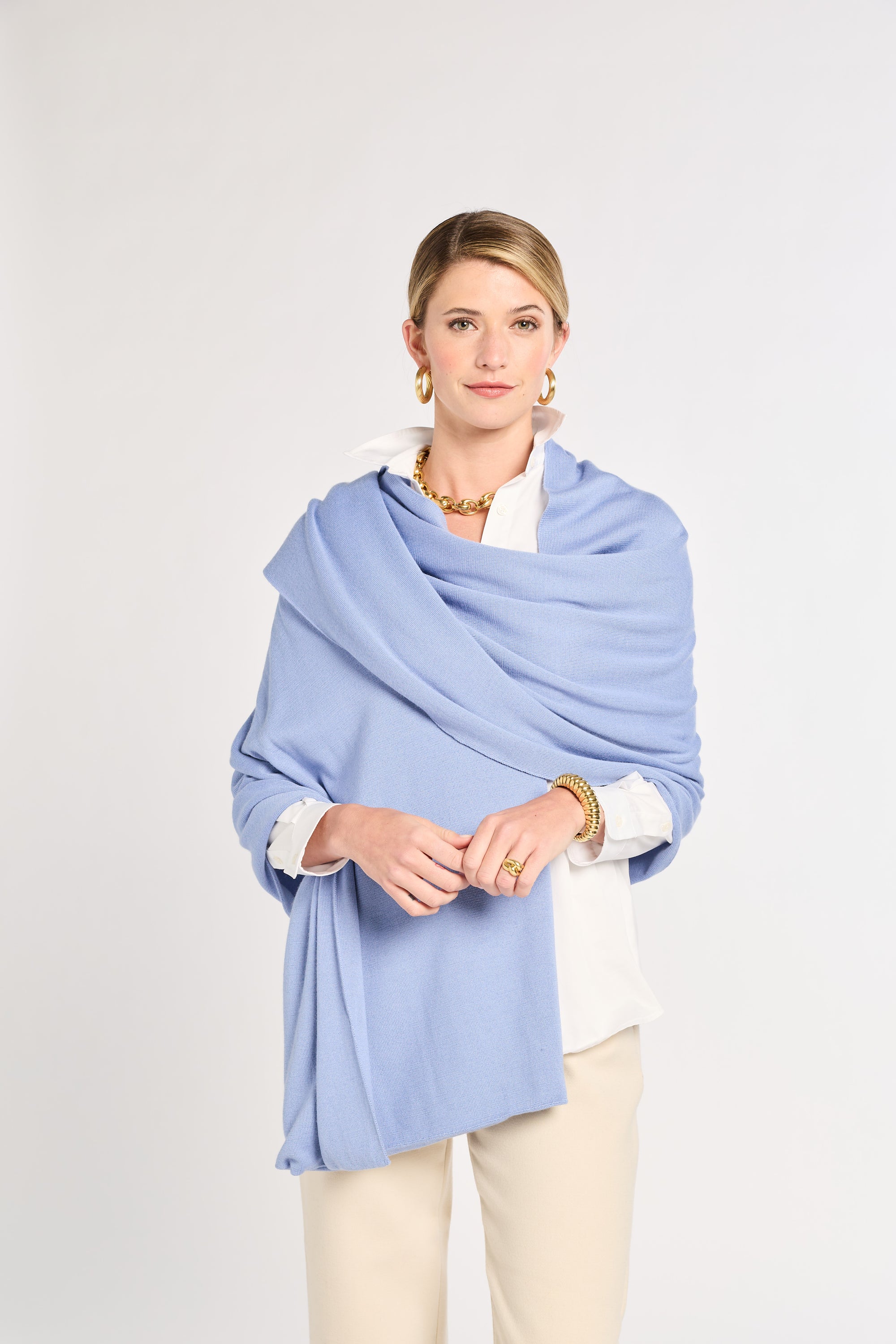 Woman wearing a light blue shawl over a white shirt on a plain background