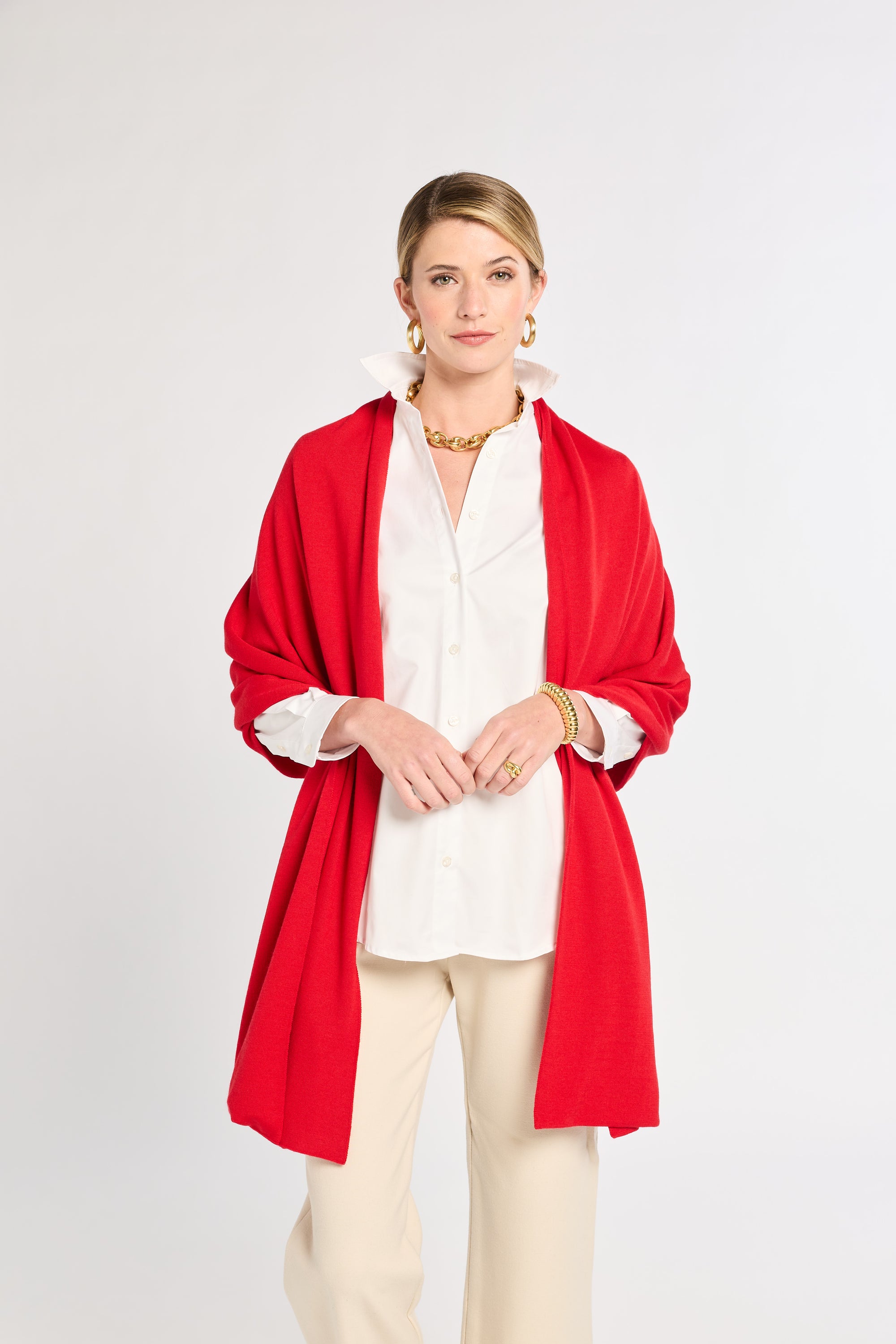 Woman wearing a red cardigan over a white shirt and beige pants on a white background
