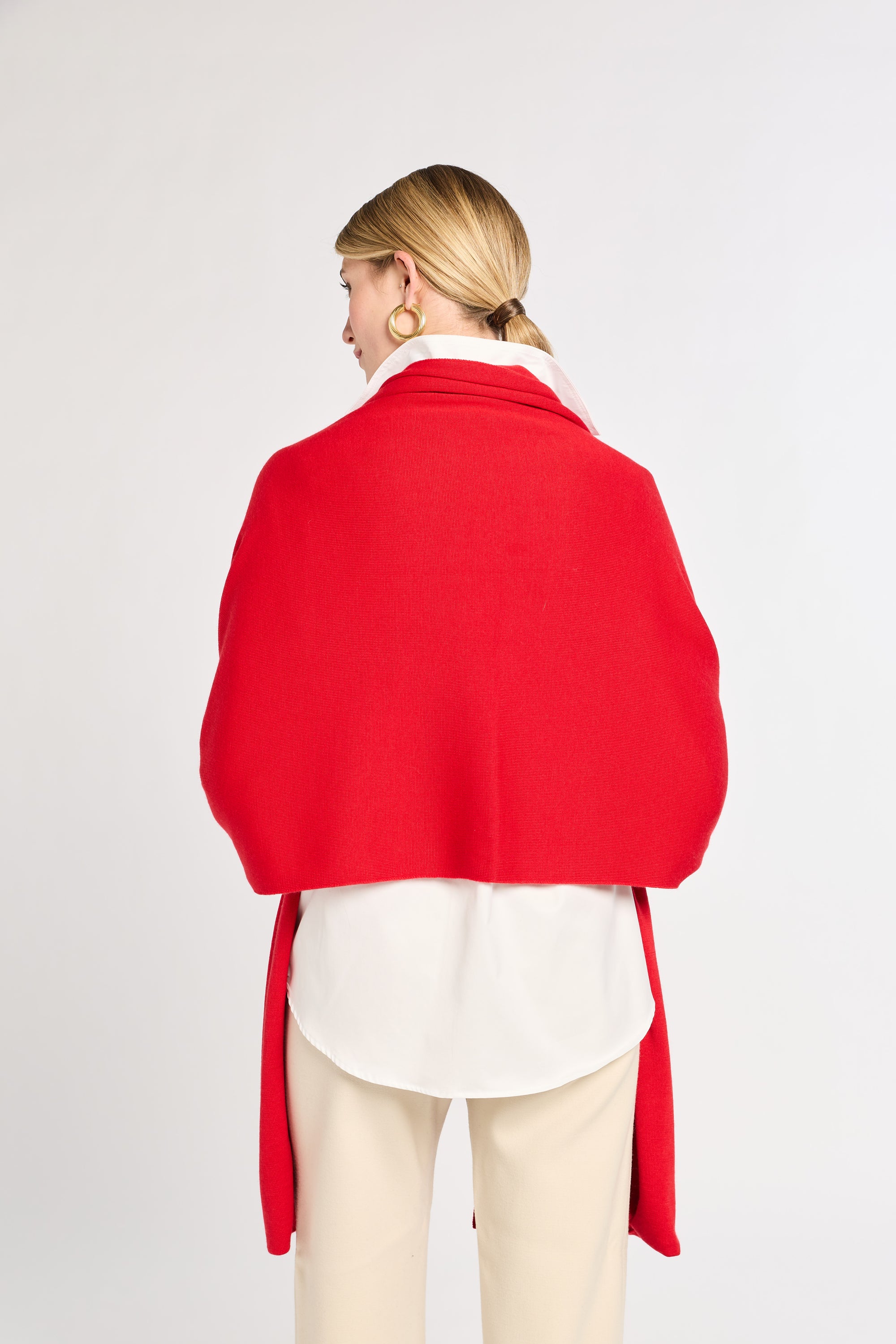 Person wearing a red shawl over a white shirt and beige pants on a light gray background