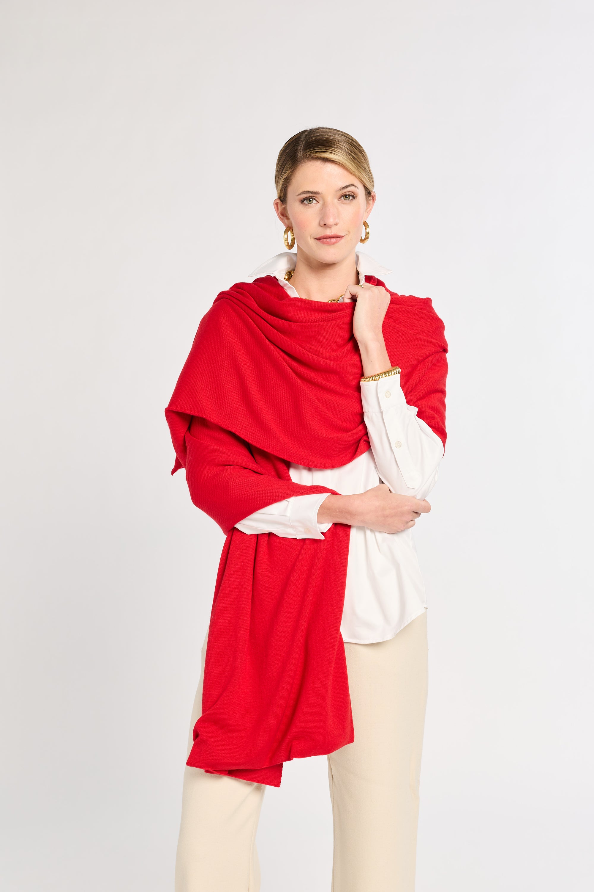 Woman wearing a red shawl over a white top and beige pants on a light gray background