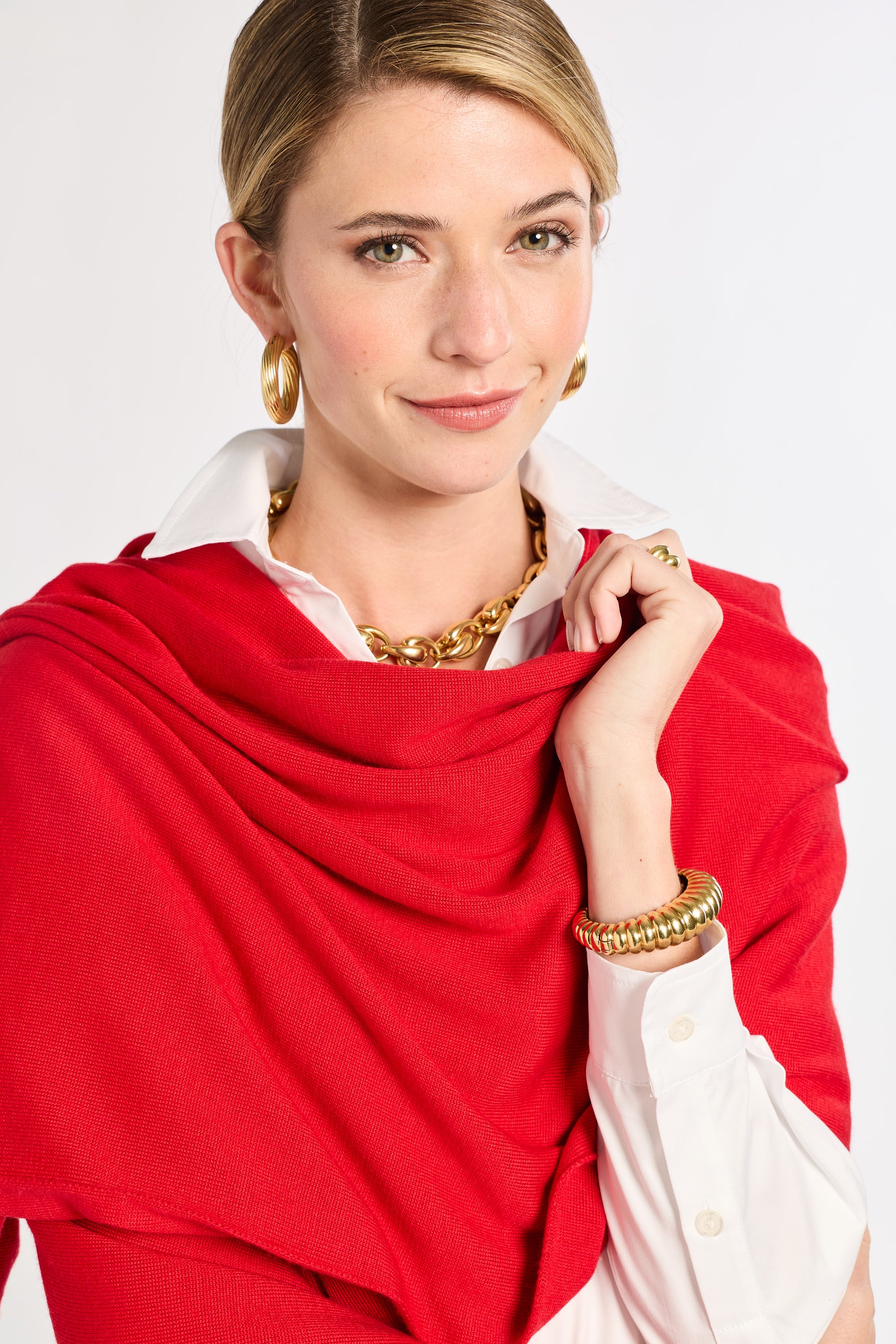 Woman wearing a red scarf, white shirt, and gold jewelry on a plain background