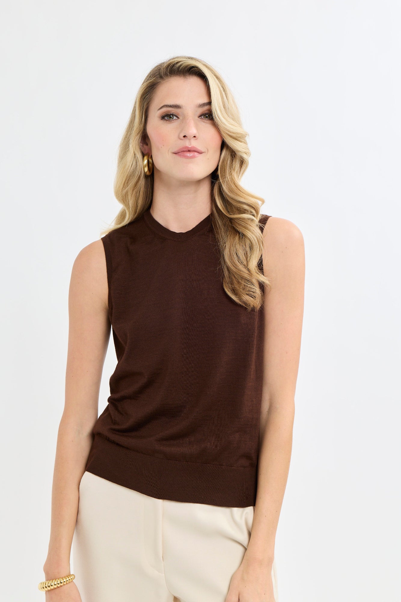 Woman wearing a brown sleeveless top and beige pants on a white background