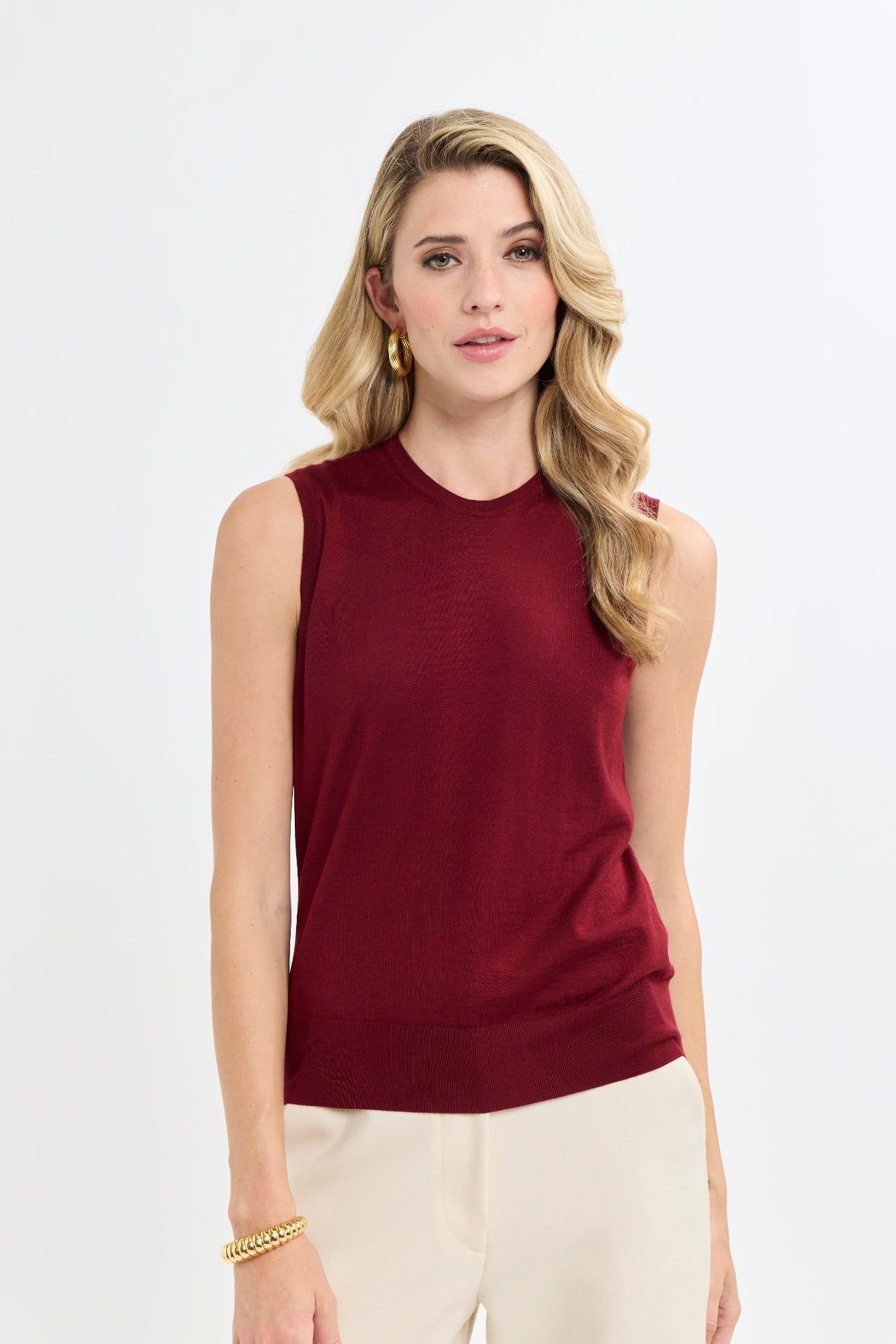 Woman wearing a burgundy sleeveless top and beige pants on a white background