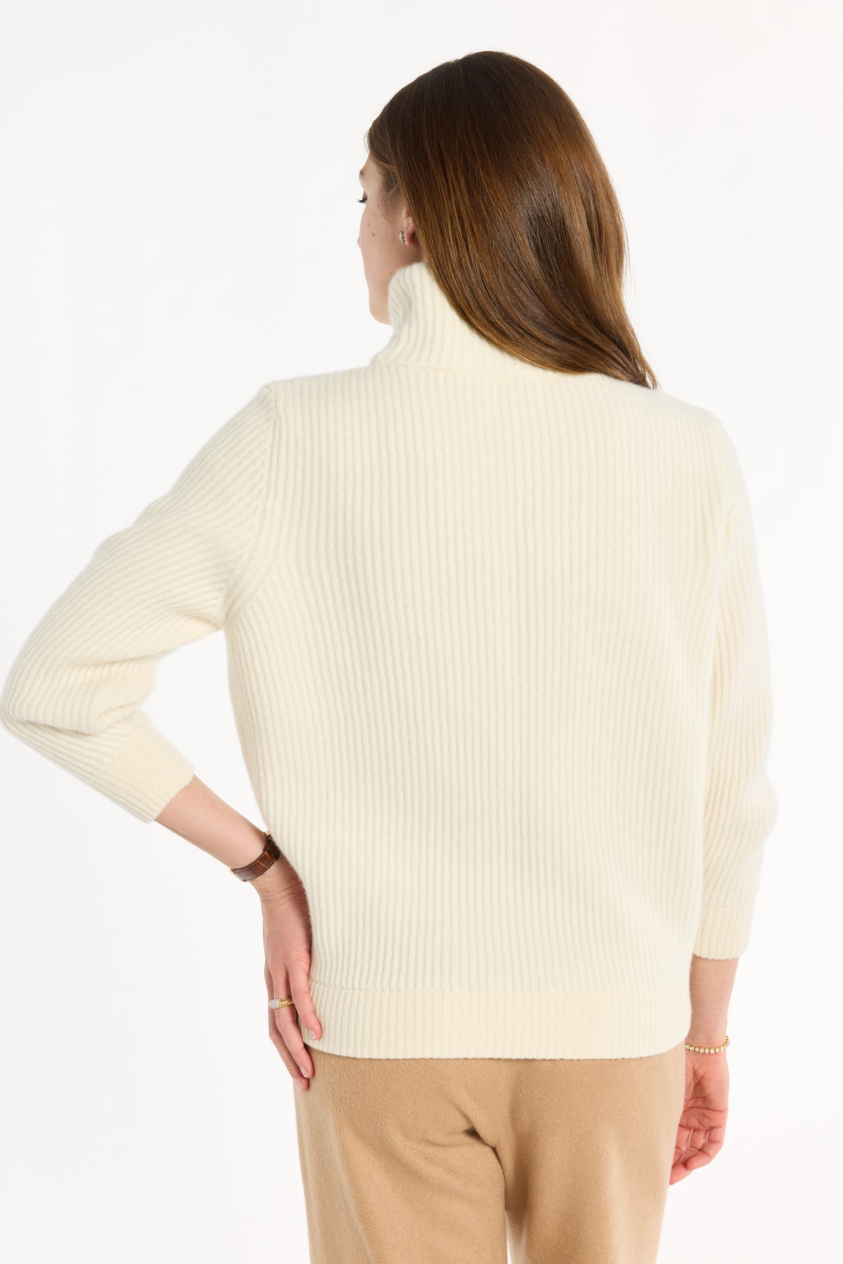 Woman wearing cream baby cashmere turtleneck with camel cashmere pants on a white background