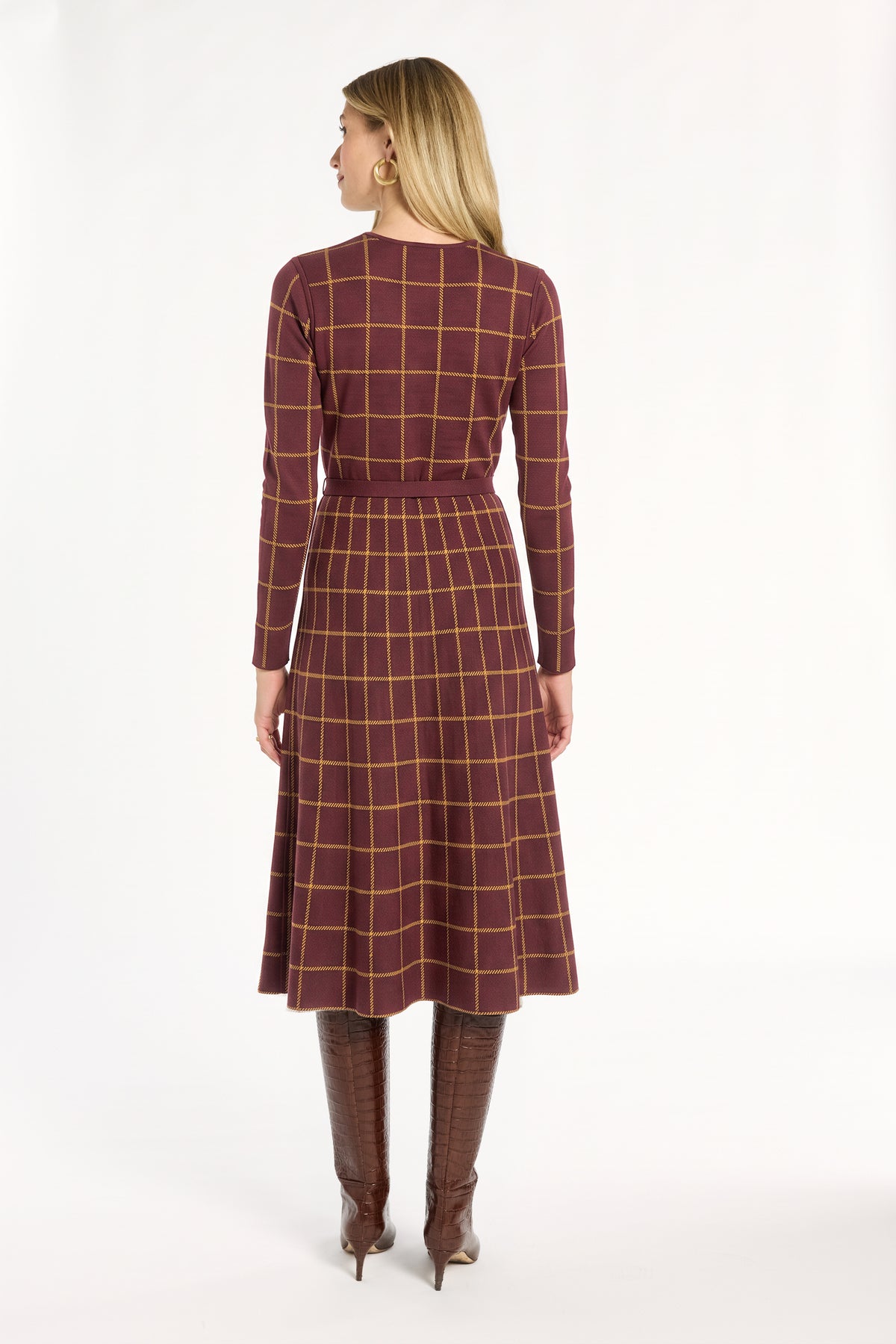 A woman modeling the cranberry side of the Windowpane Plaid Reversible Flared Skirt with the matching skirt and brown boots, back view, photographed against a plain white studio background.