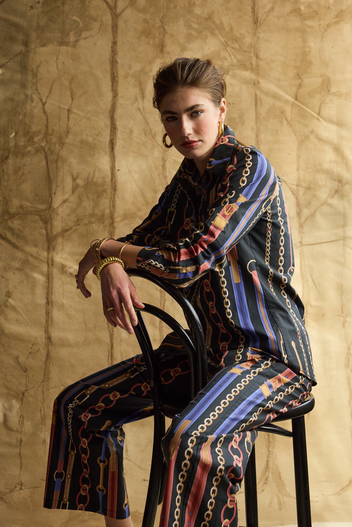 Woman modeling chain linked pattern pants with a tan background