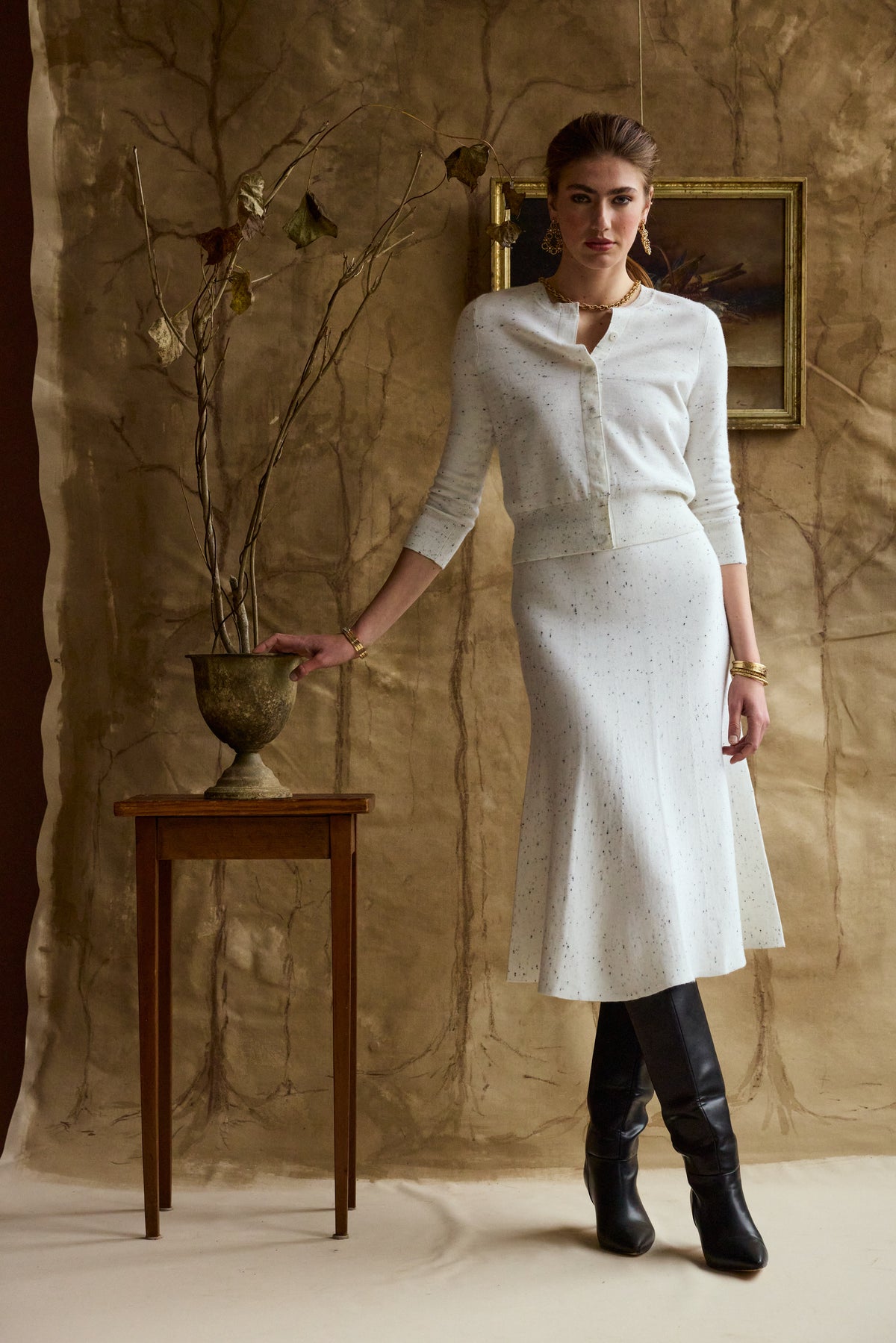 Woman modeling a white flecked skirt and cardigan on a tan backdrop