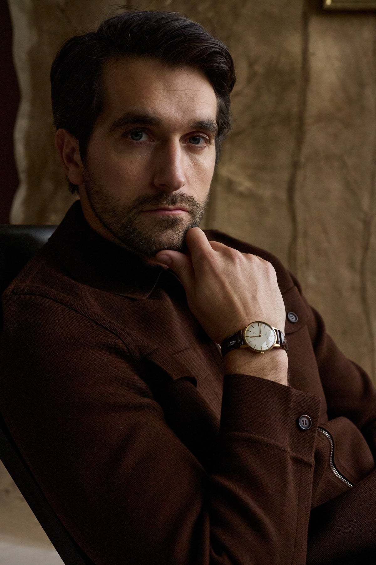 Man modeling a chocolate brown shacket and wearing a watch on a tan background