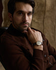Man modeling a chocolate brown shacket and wearing a watch on a tan background