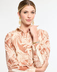 Woman wearing a patterned dress with gold earrings on a white background