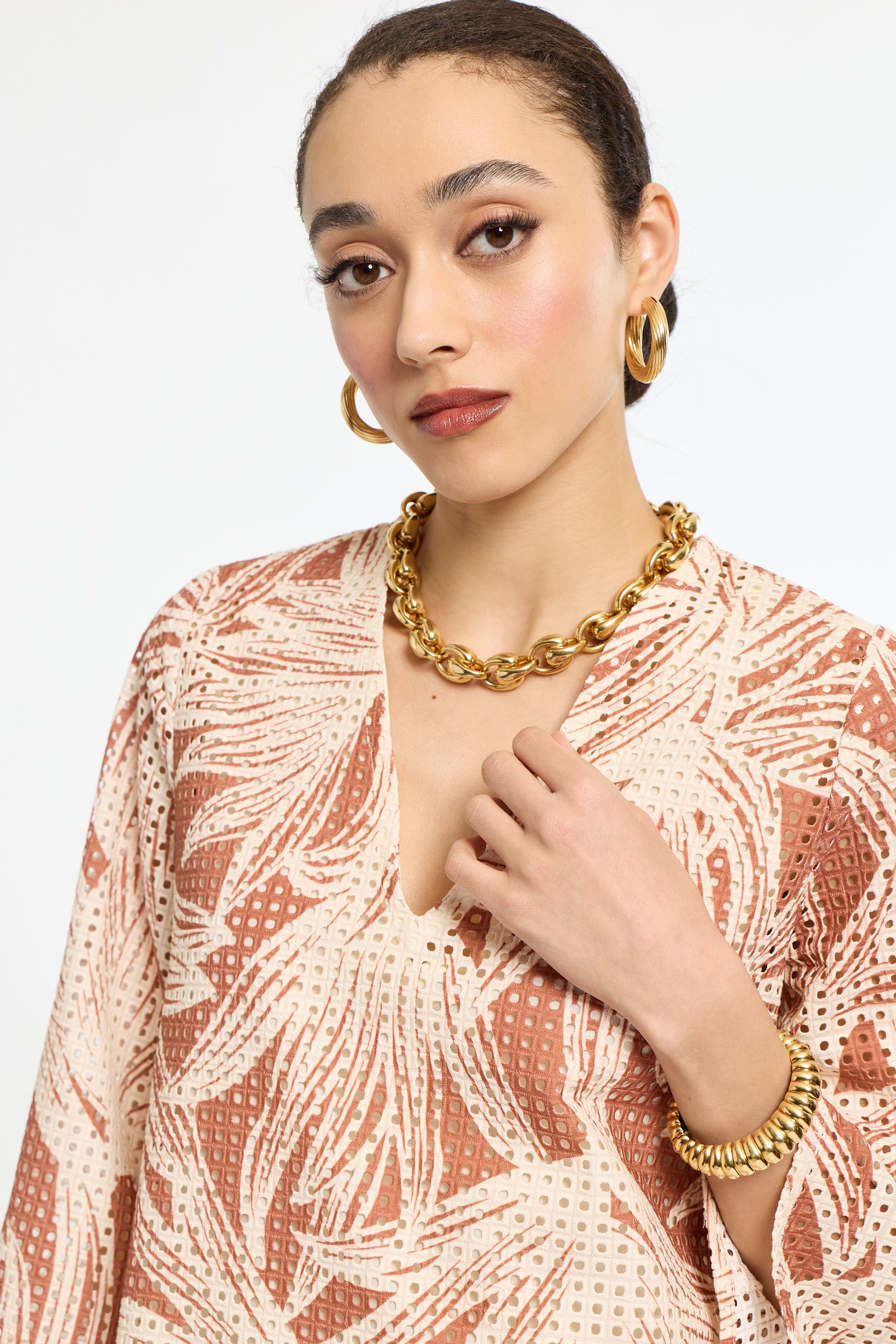 Woman wearing a patterned top and gold jewelry on a white background