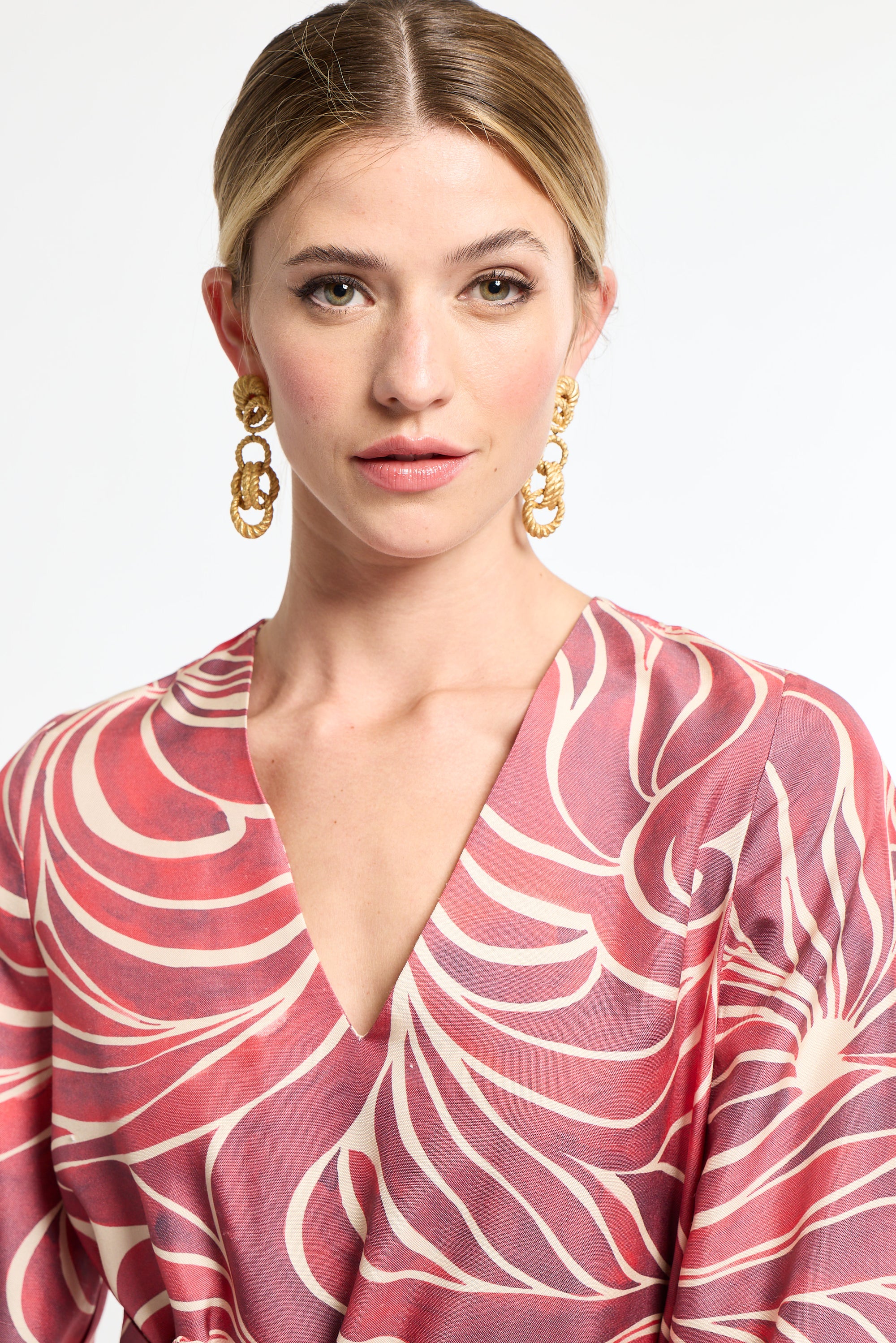 Woman wearing a pink and white patterned dress with gold earrings on a light background