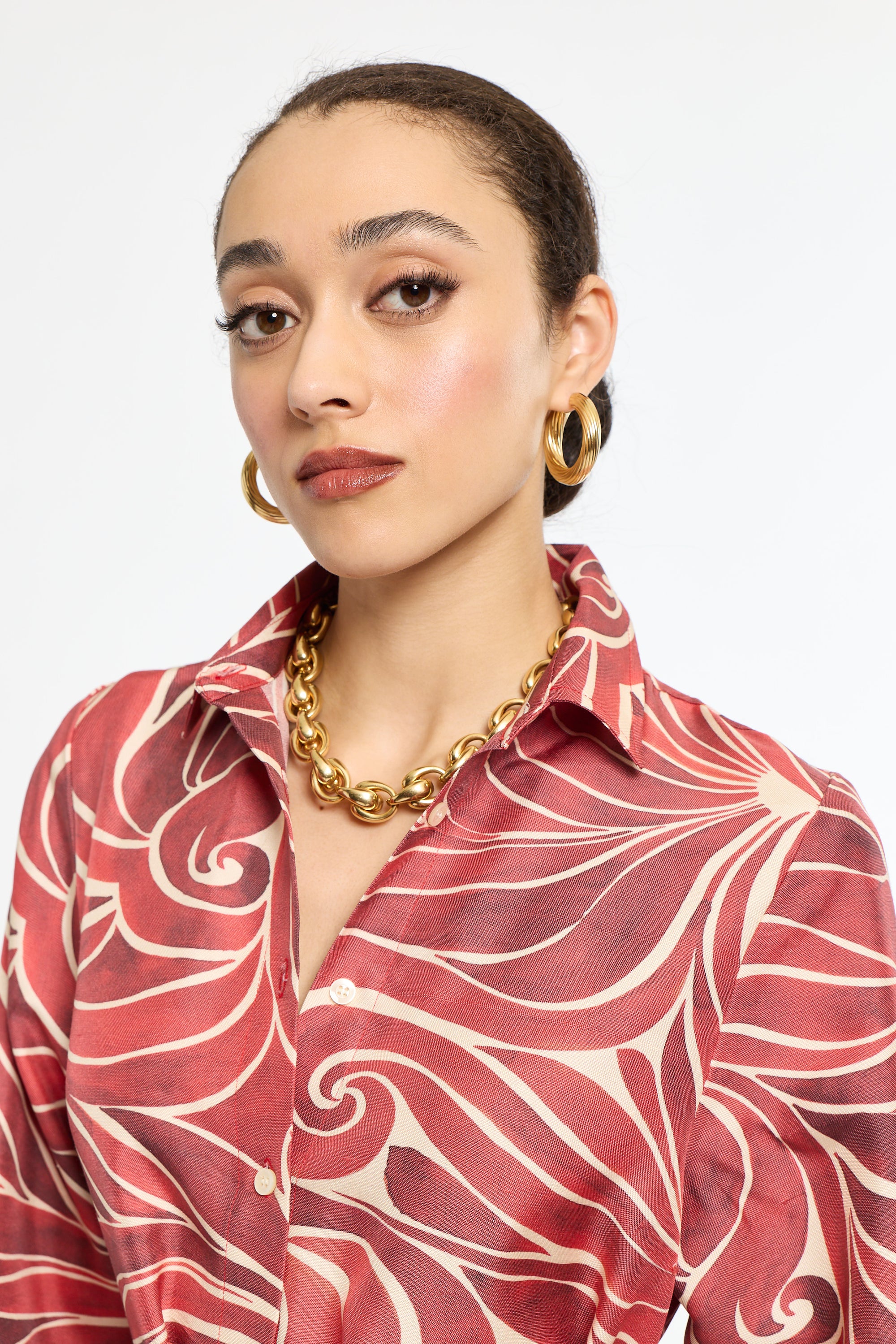 Woman wearing a red patterned shirt with gold jewelry on a white background