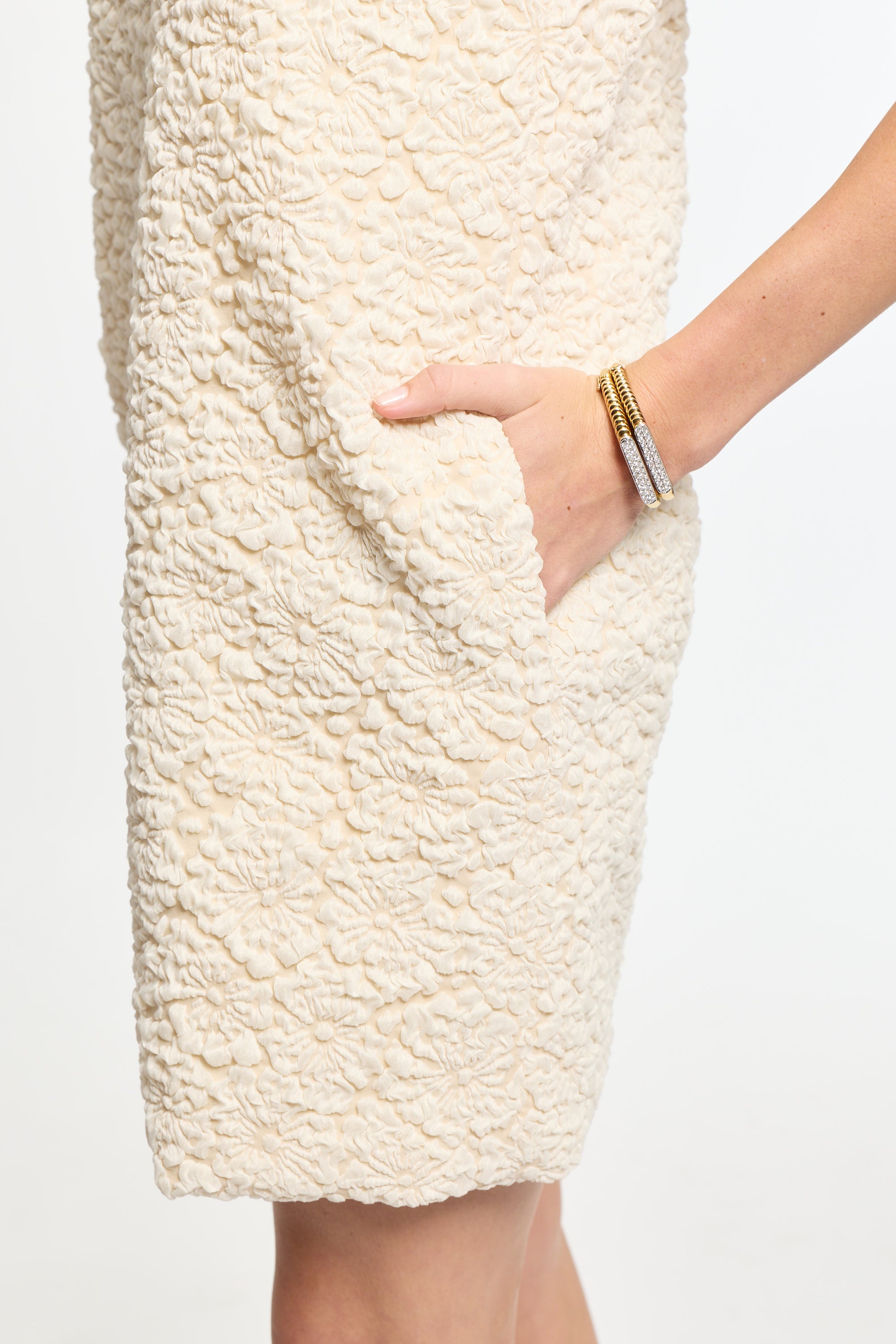 Close-up of a textured cream-colored skirt with a hand touching it on a white background