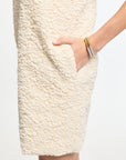 Close-up of a textured cream-colored skirt with a hand touching it on a white background