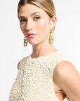 Woman wearing gold earrings and a textured cream dress against a white background