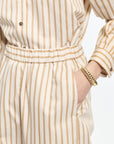 Person wearing a beige and white striped outfit with a gold bracelet on a plain background