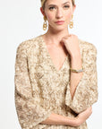 Woman wearing a gold patterned blouse on a white background