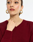Woman wearing gold hoop earrings and a red sweater on a white background
