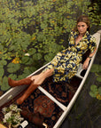 Woman in a patterned dress sitting in a boat on a waterway with greenery.