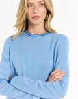 Woman wearing a light blue ensemble with dark blue trim against a white backdrop.
