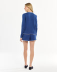 Woman showcasing a blue long-sleeve top and shorts set, photographed in a bright studio setting.