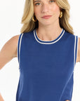 Woman wearing a blue sleeveless top with white trim on a white background