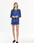 Woman wearing a blue knit set with white piping on a white background