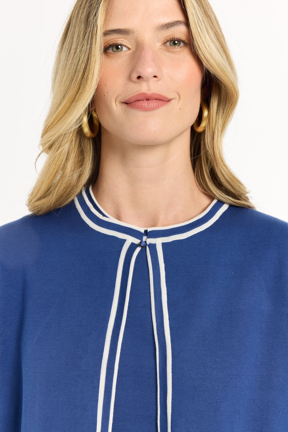 Woman wearing a blue top with white trim on a plain background