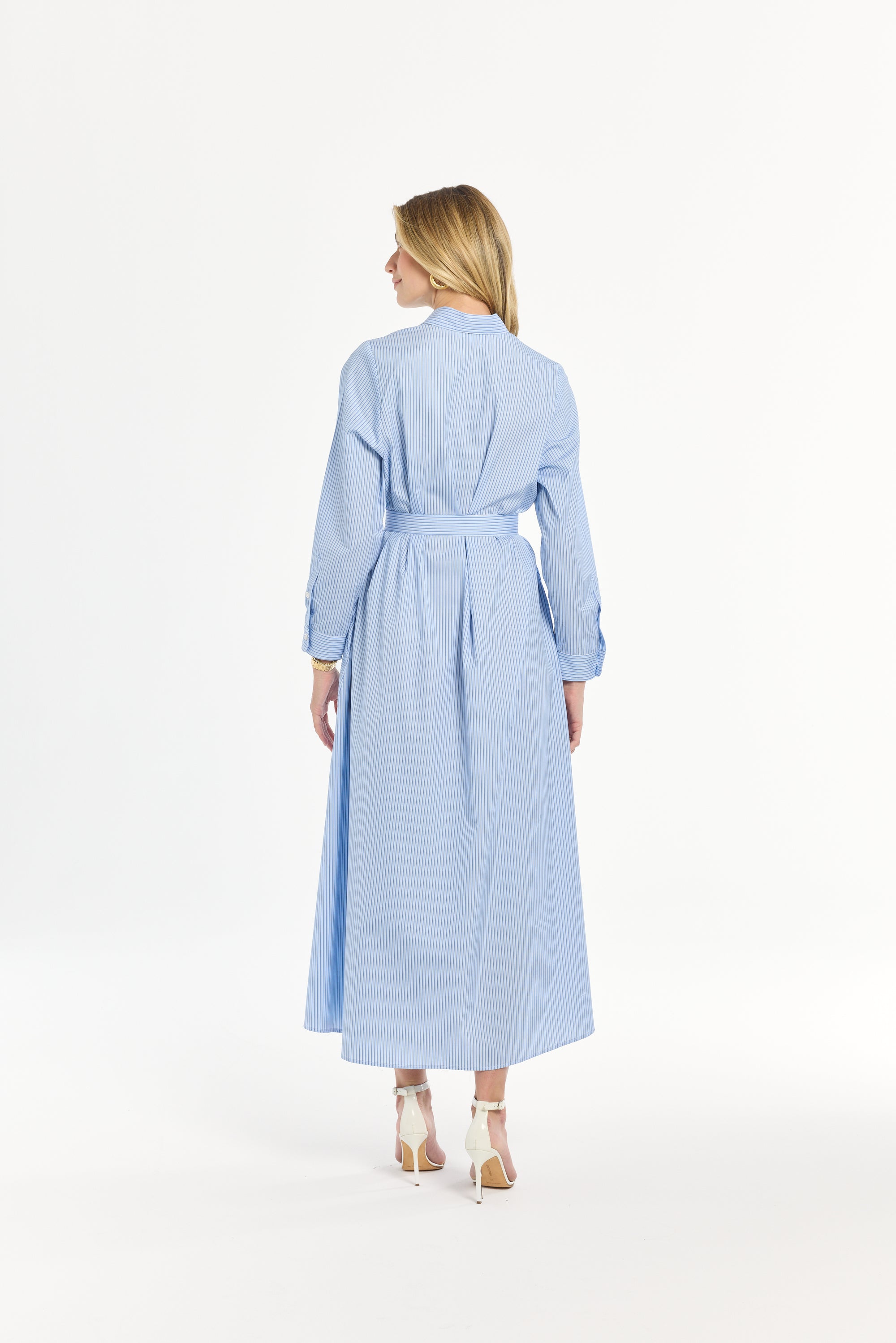 Woman wearing a light blue striped dress with a tie belt on a white background