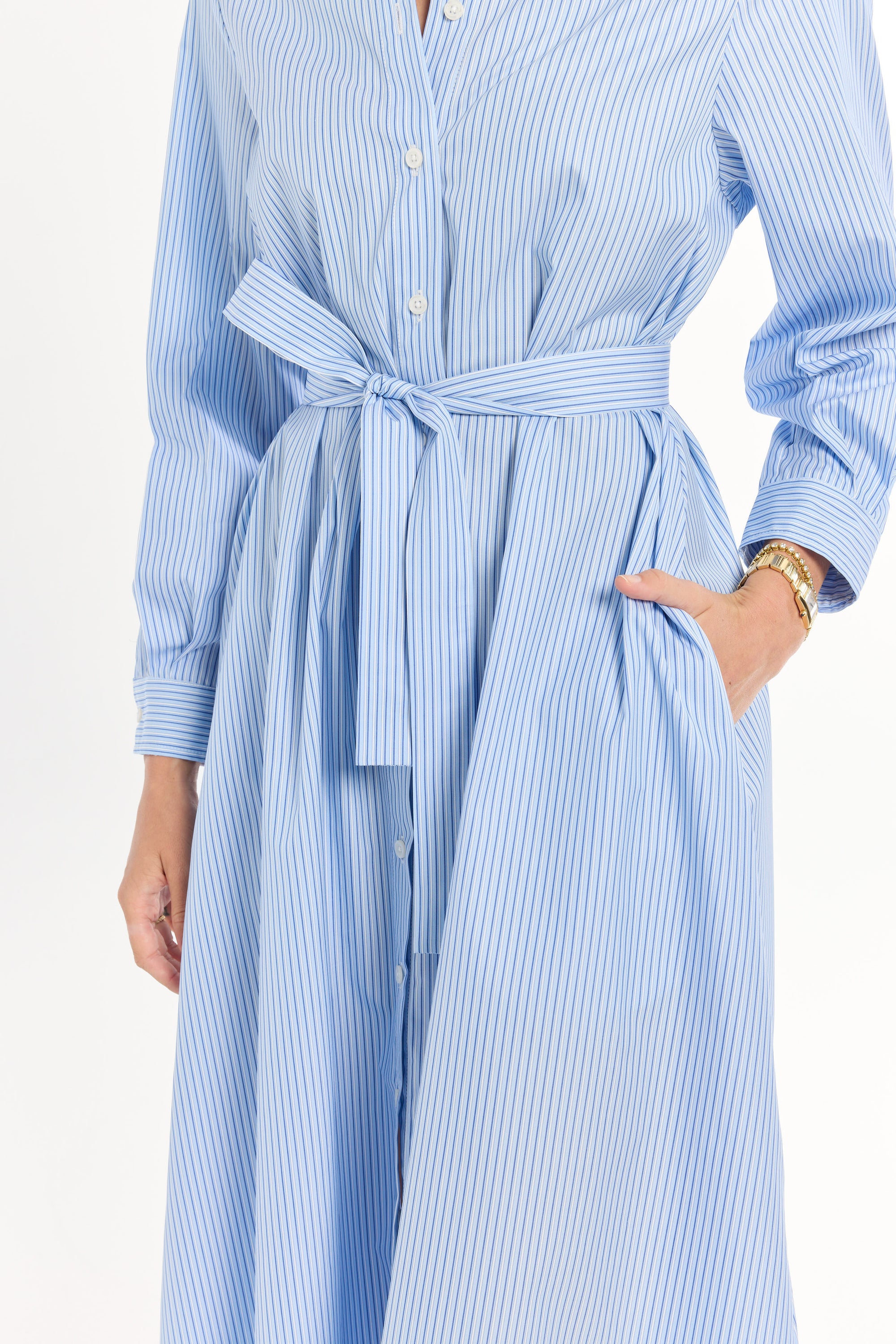 Woman wearing a blue and white striped dress with a belt, standing against a light background.