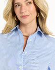 Woman wearing a blue striped dress and gold hoops with a plain background