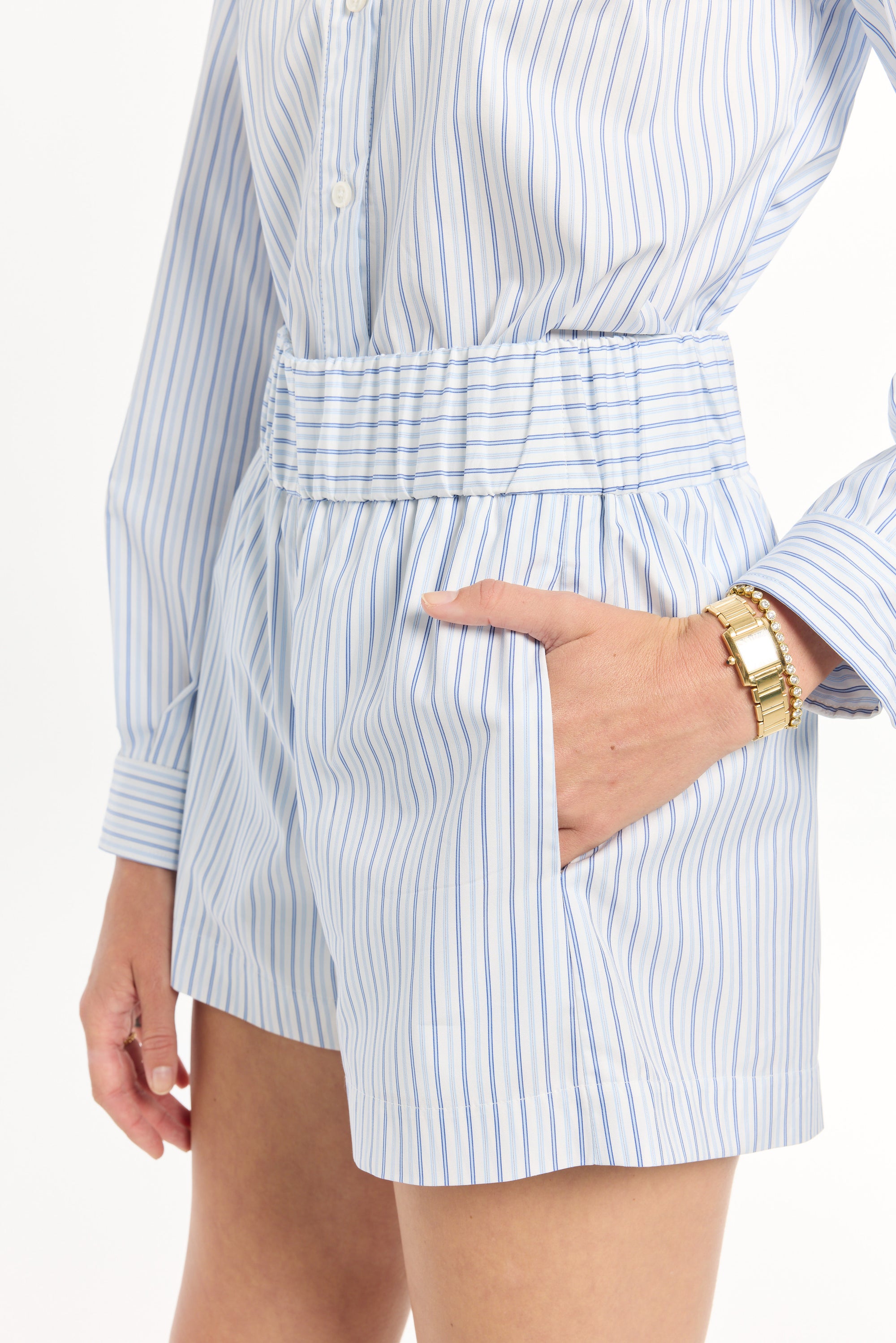 Person wearing a light blue and white striped shirt with shorts, with hand in the pocket