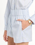 Person wearing a light blue and white striped shirt with shorts, with hand in the pocket