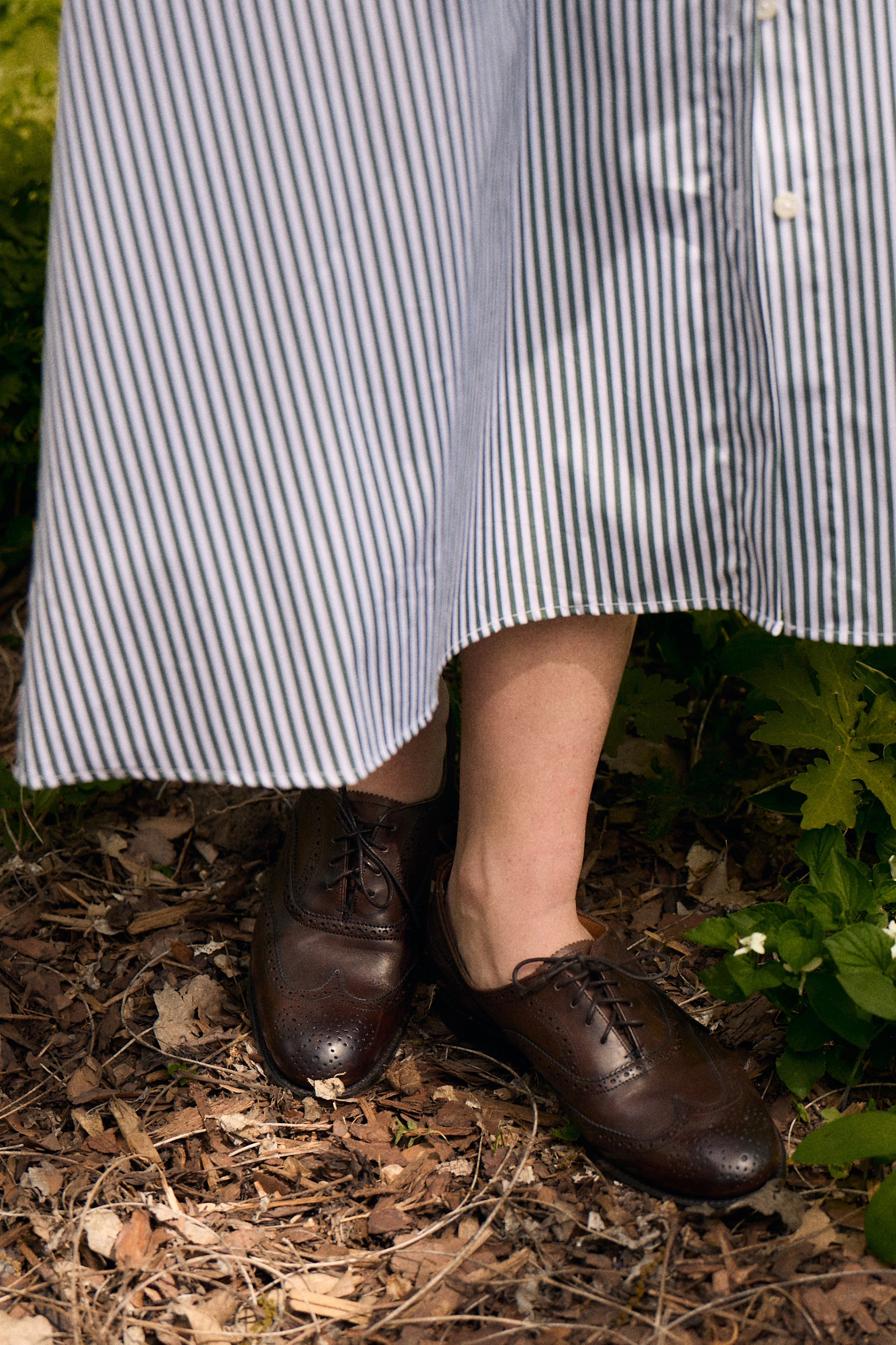 Person wearing a striped dress and brown shoes standing in a garden.