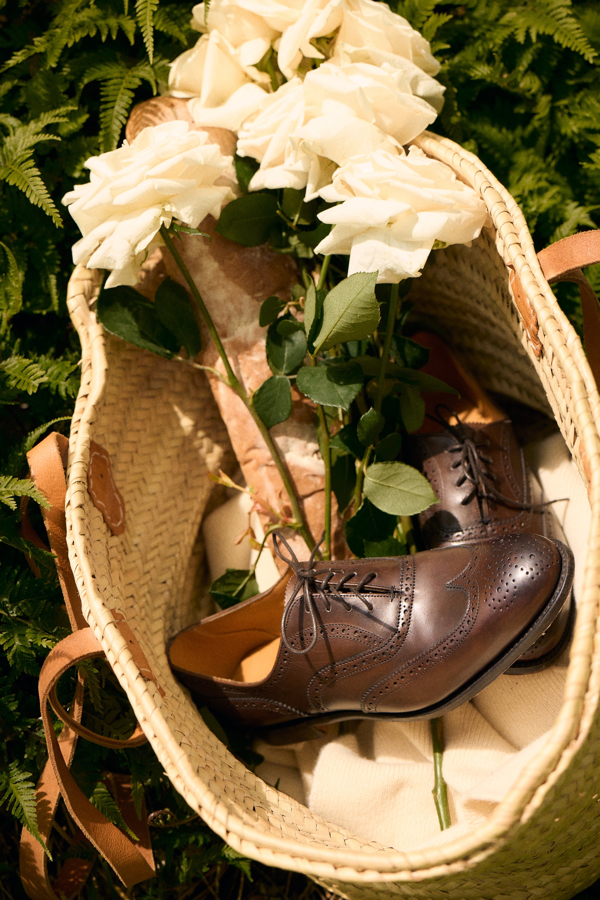 Brown dress shoes in a woven basket with white flowers and green leaves on a natural background