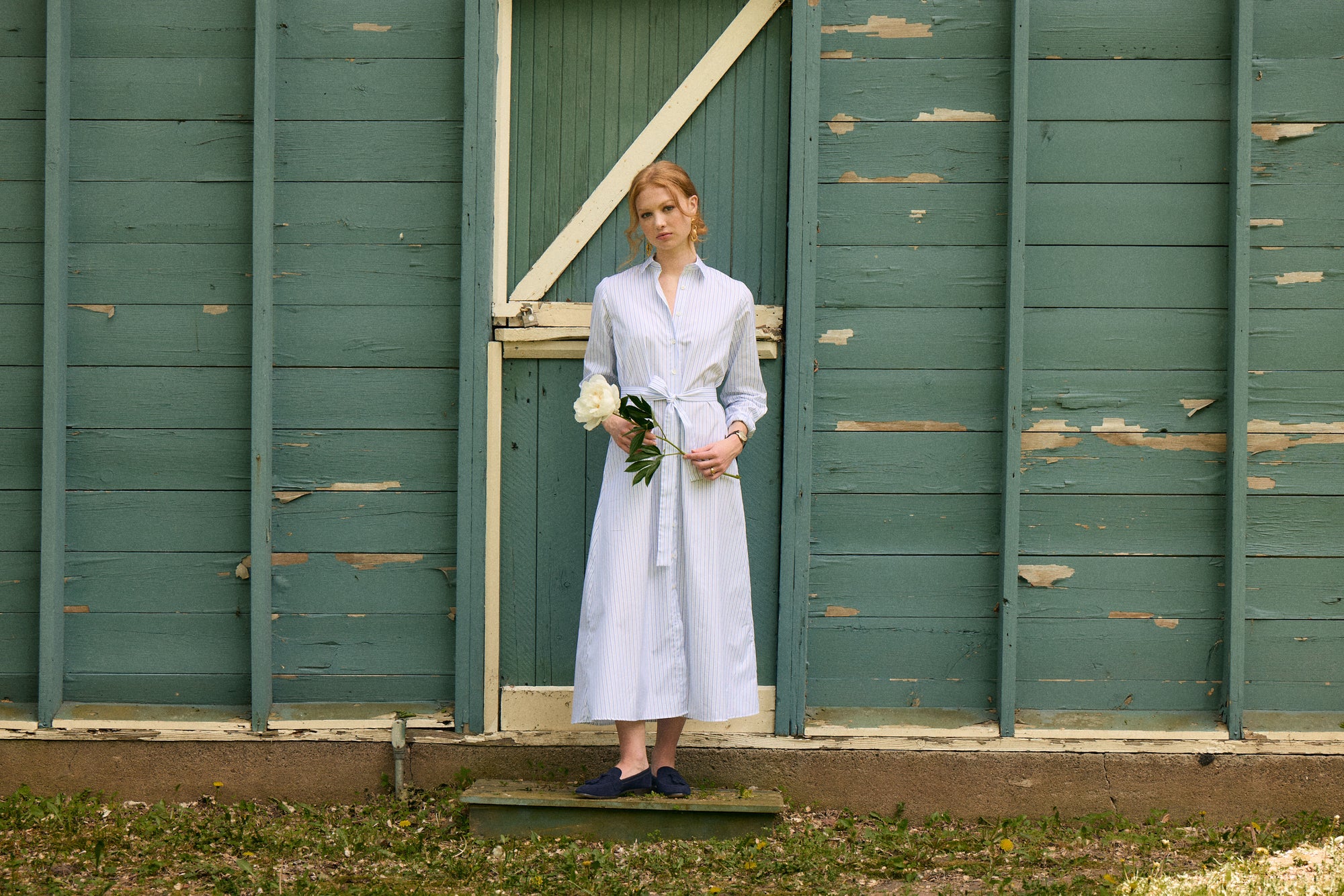 Woman in a light blue dress standing in front of a green wooden door.