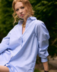 Woman wearing a light blue striped shirt outdoors with greenery in the background