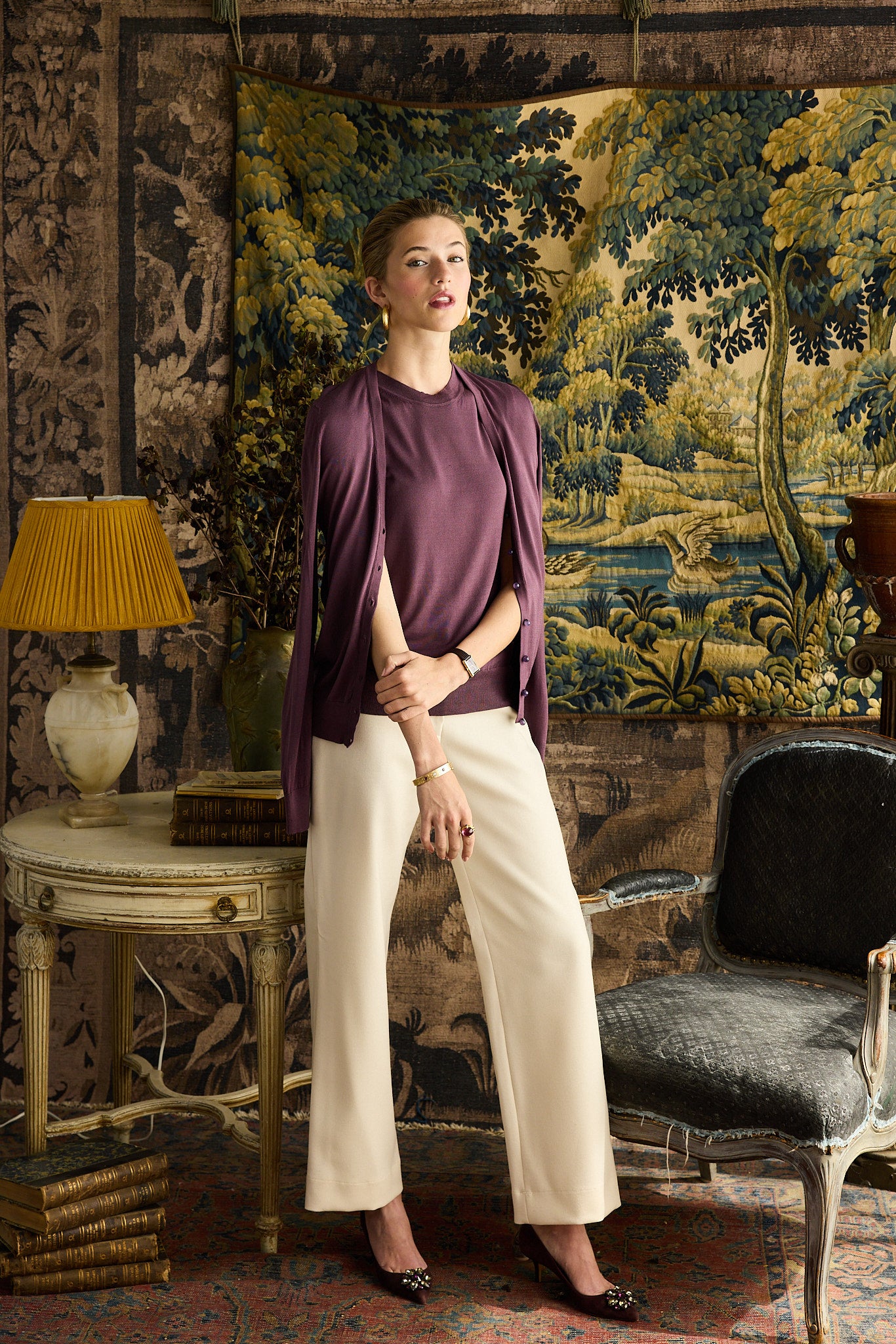 Woman standing in a room with decorative wall tapestry and vintage furniture.